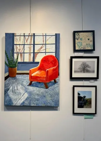 image of a painting of an orange armchair by a window and other framed artworks