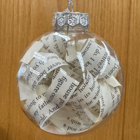 Clear round holiday tree ornament filled with curled strips taken from the pages of books