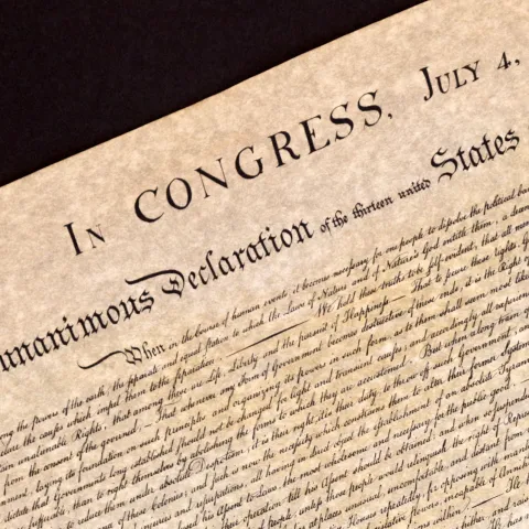 An image of an old piece of pachment with In Congress July 4 at the top and Unanimous Declaration under it with a lot of smaller indecipherable calligraphy under that