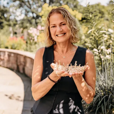 A photograph of a blond woman holding a crown and wearing black