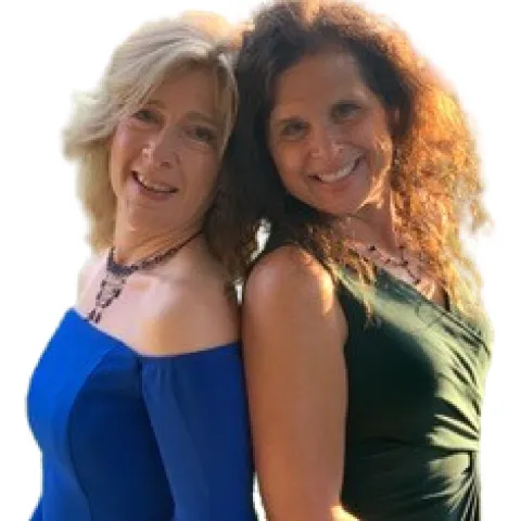 A blond woman in a blue dress with her back to a brunette woman in a green dress