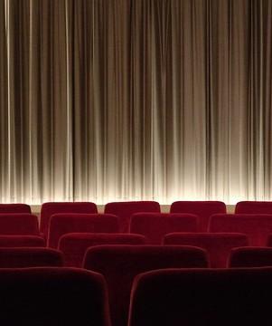 Image of a theater with red seats and a brown curtain